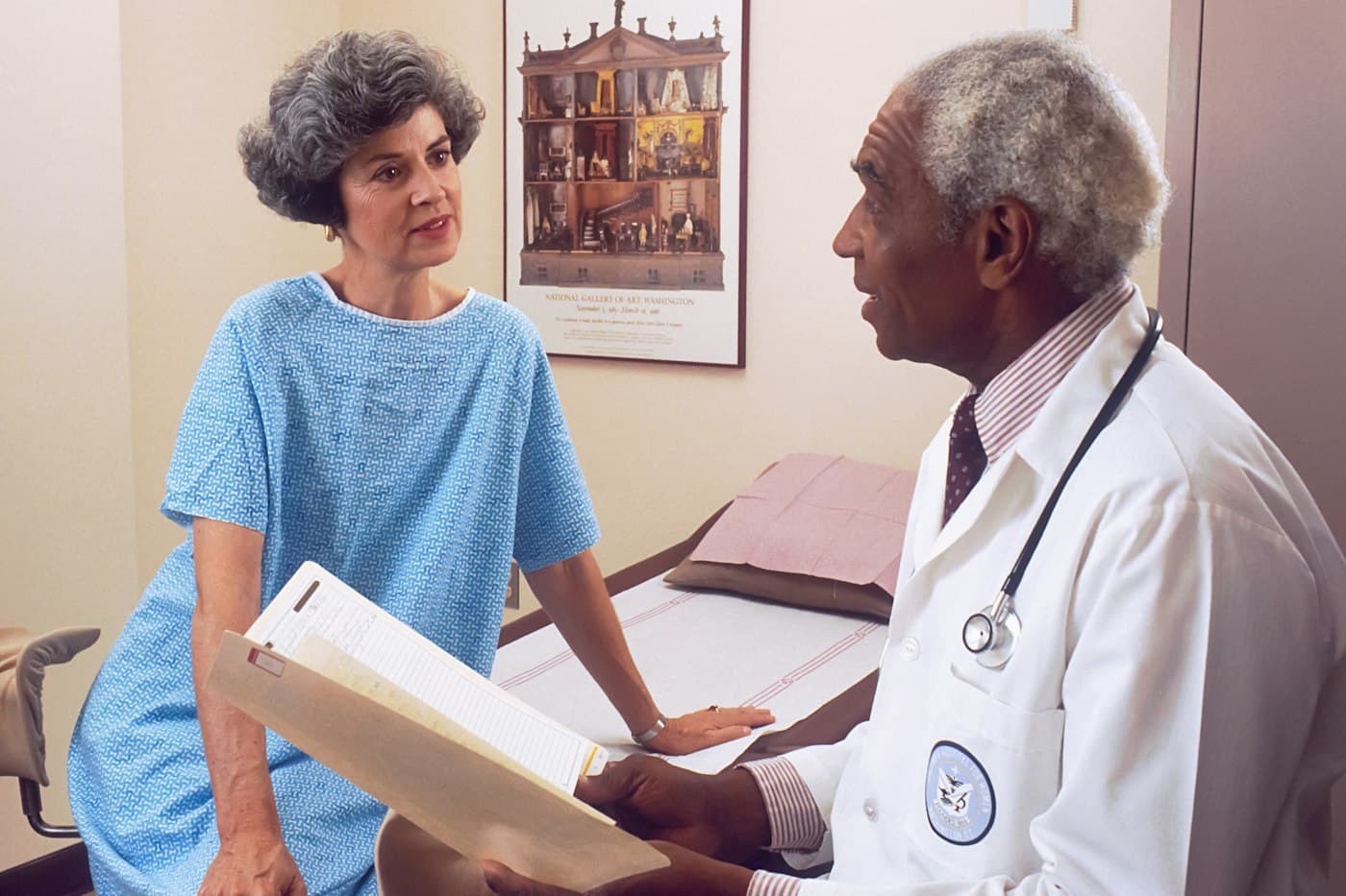 A physician reviewing paperwork with an older patient in an exam room